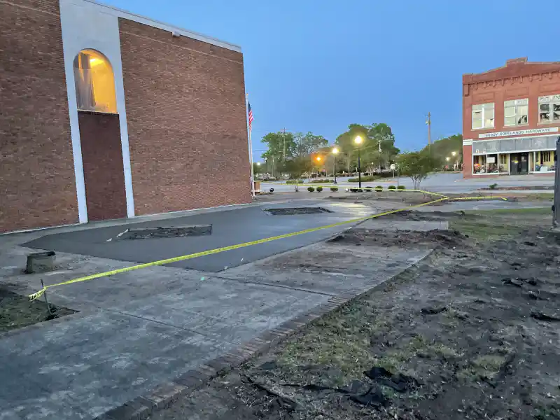 New concrete sidewalk and kerb work in front of a row of commercial storefronts.