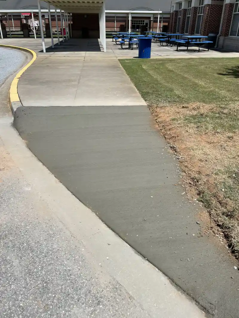A concrete accessible ramp and sidewalk with a detectable warning surface panel on a campus walkway.