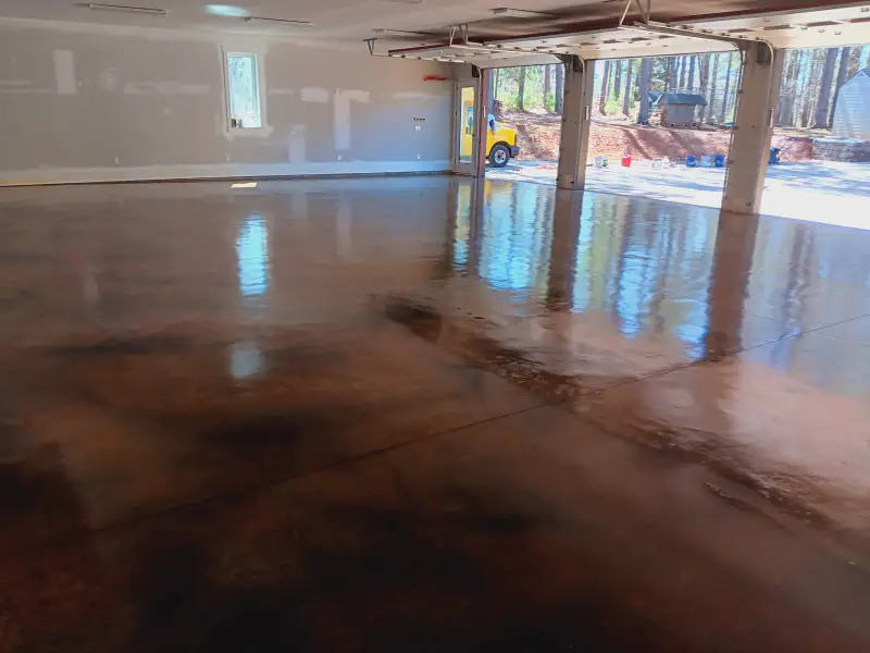A large garage interior with a mottled brown acid-stained and sealed concrete floor, reflecting three open garage doors.