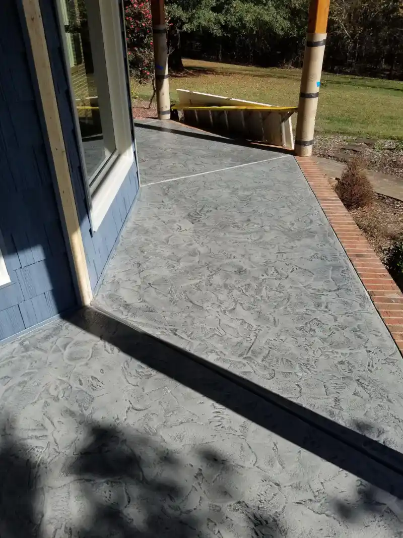 A grey mottled-texture overlay applied to a porch slab and lower step at a blue-clad house with a brick border edge.