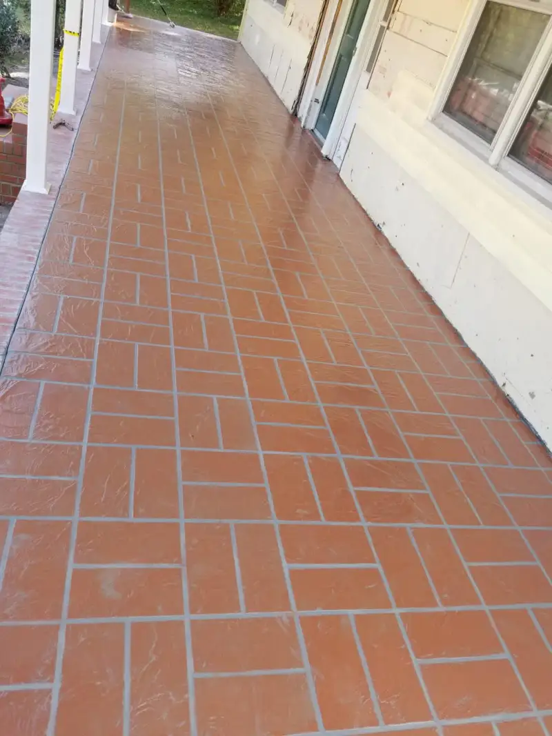 A long porch floor finished with a terracotta brick-pattern overlay with grey jointing, wet from a freshly applied sealer.