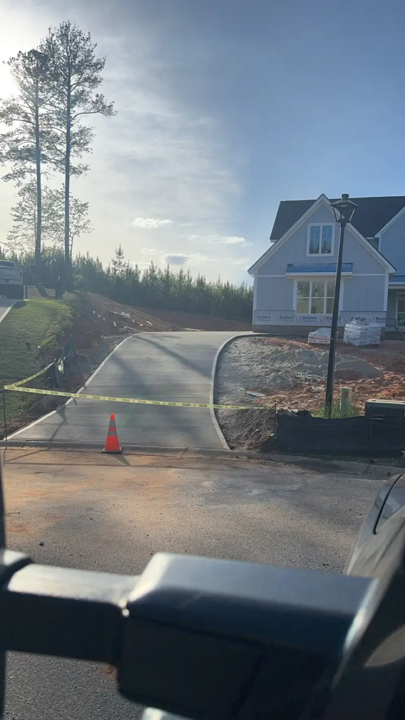 A newly poured driveway in front of a house under construction wrapped in building paper.