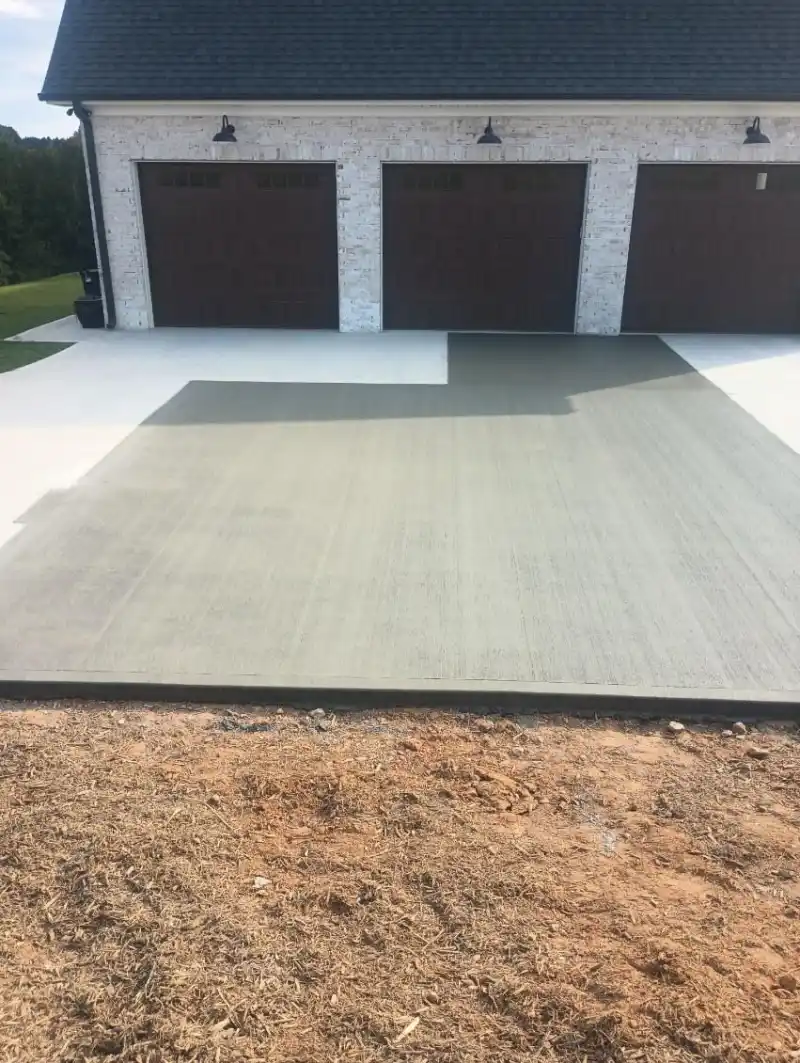 A freshly poured concrete apron meeting an older cured slab in front of a three-car garage.