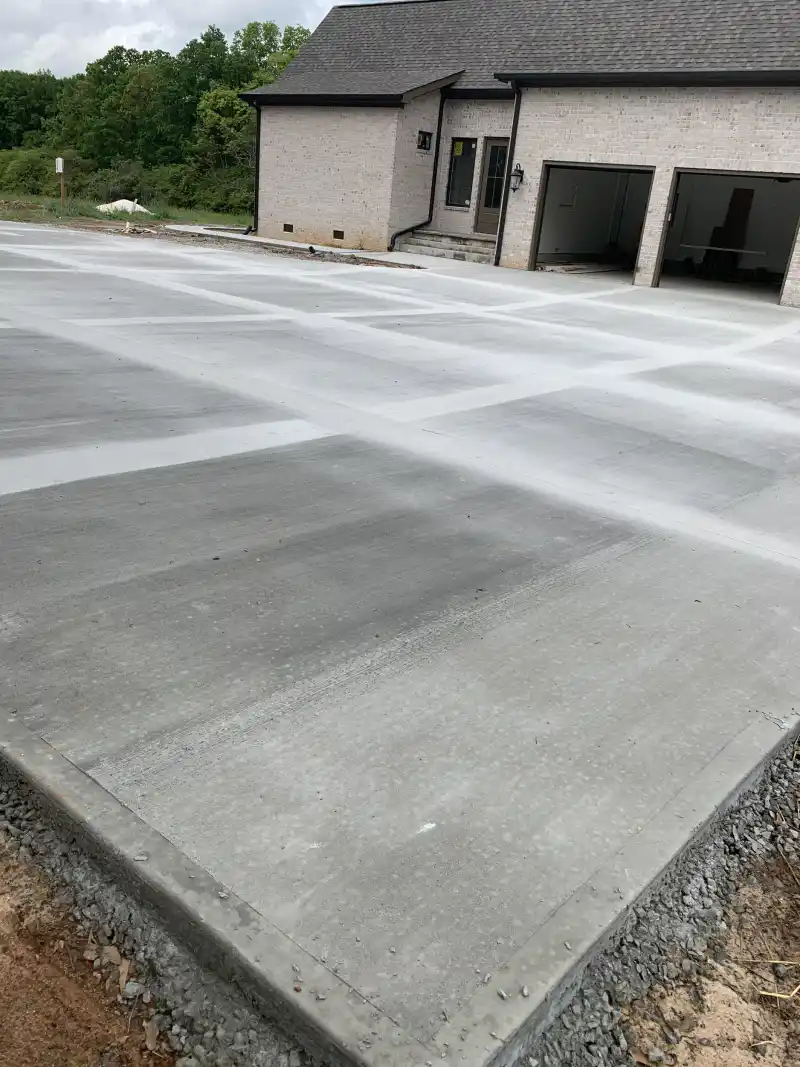 A large concrete parking pad and driveway in front of a brick house with its garage doors open.