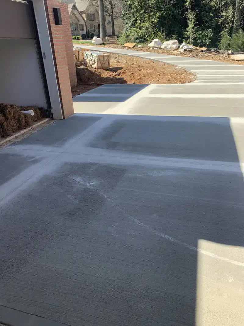 A newly poured driveway section, darker than the adjoining cured concrete, running beside a brick garage.