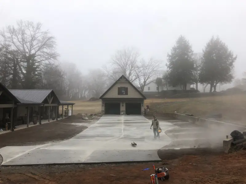 A concrete driveway photographed in morning fog, with a worker walking along the slab.