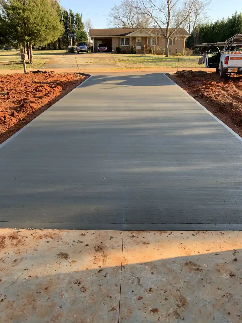 A concrete driveway at a residential property with parked vehicles and a work truck alongside.