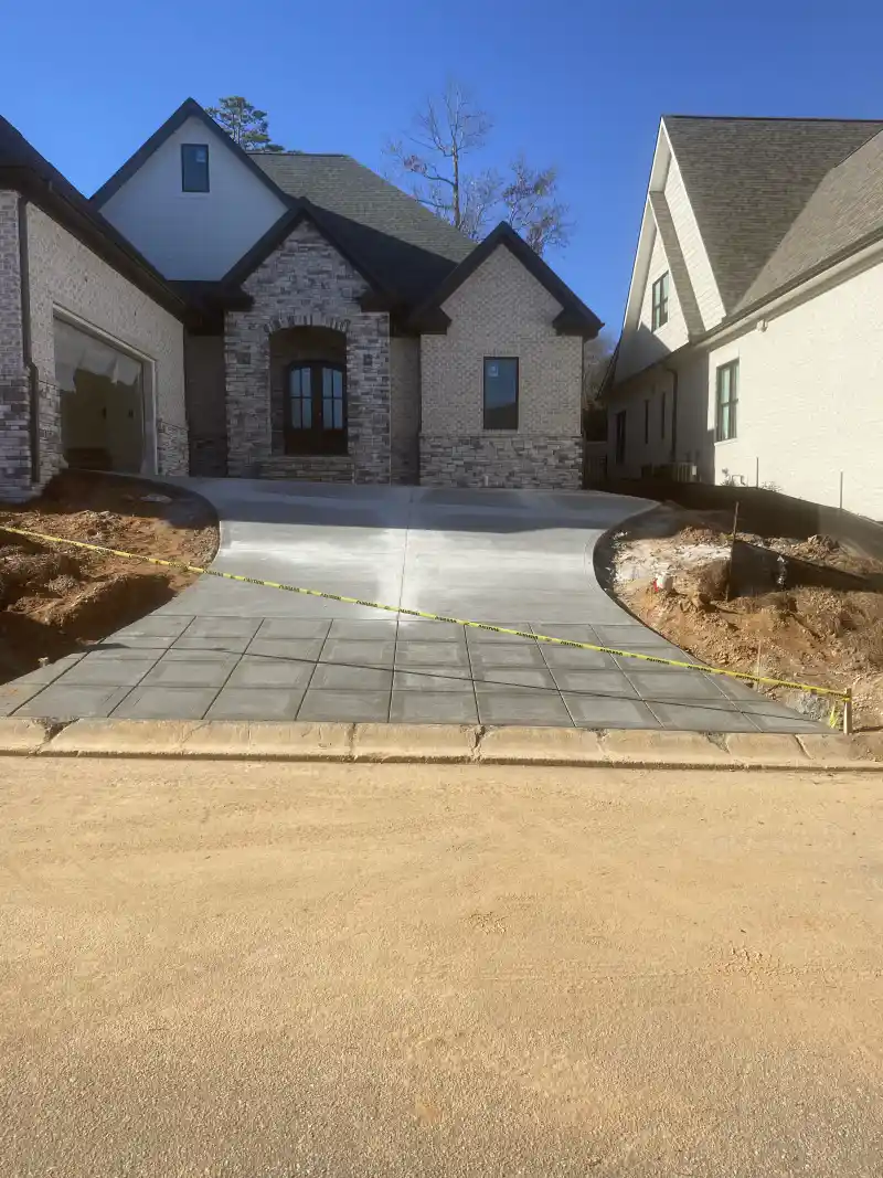 A concrete driveway apron with a scored decorative border, leading to a brick house.