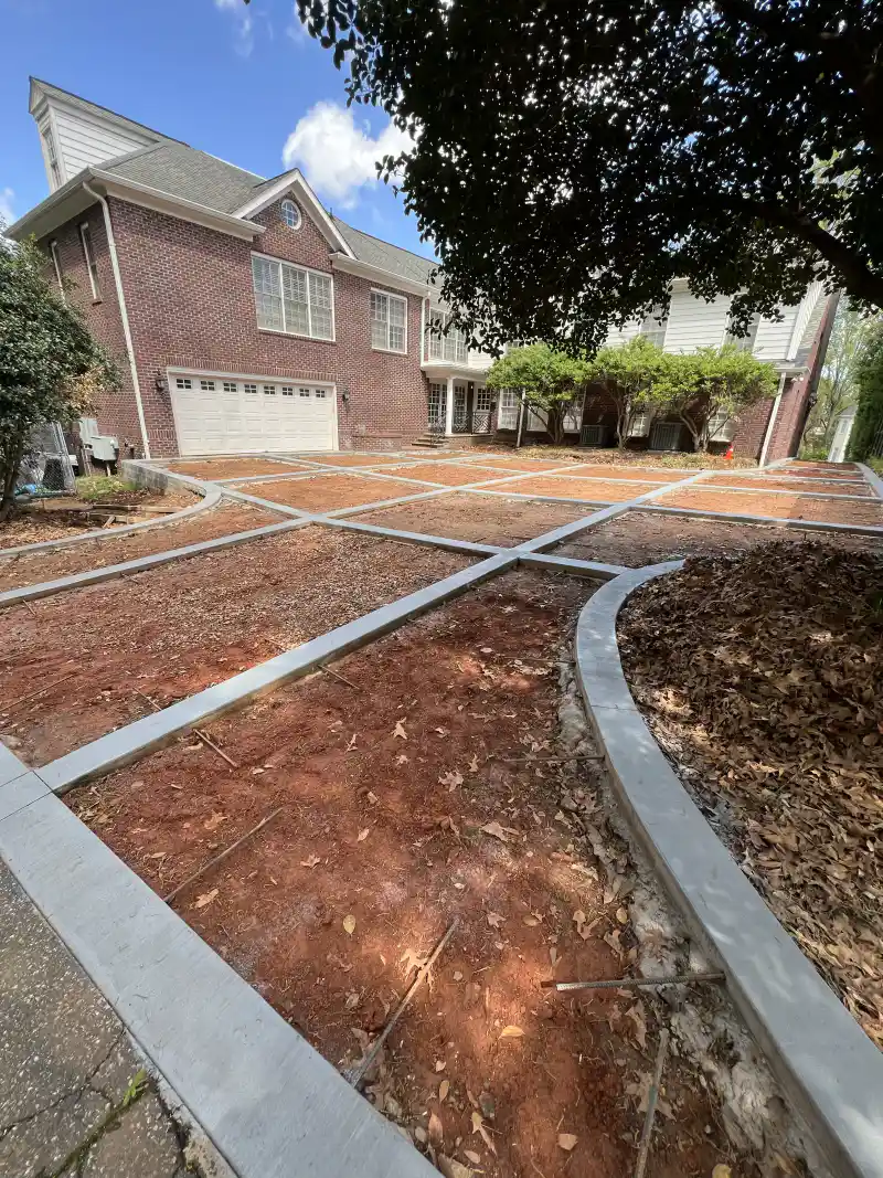 Timber forms set out over graded ground marking a driveway ahead of the concrete pour, with a brick house behind.