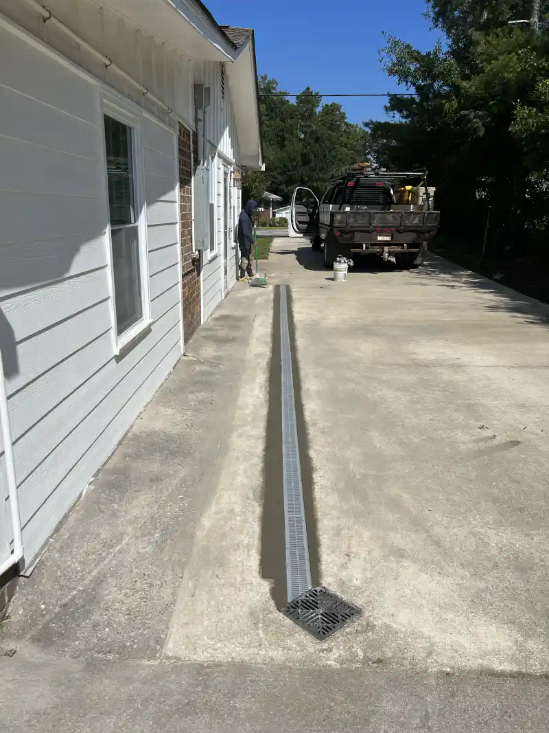 A linear trench drain channel set into a concrete driveway slab.