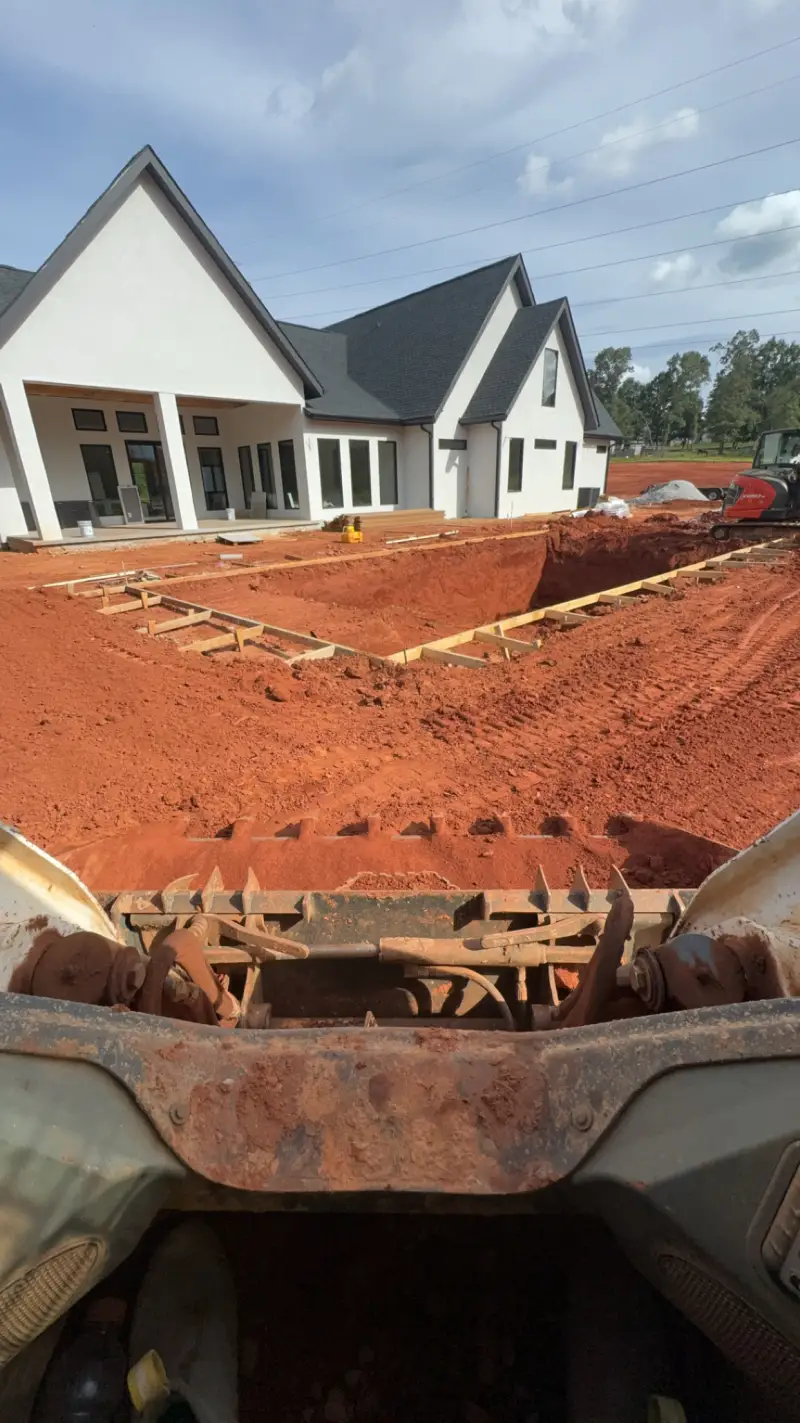 An excavated site area photographed past the raised bucket of an earthmoving machine.