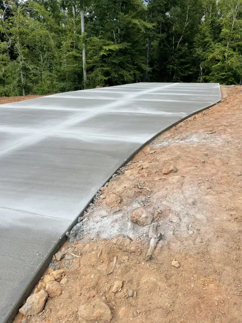 A newly poured concrete driveway curving through woodland, showing a clean thickened slab edge against red soil.