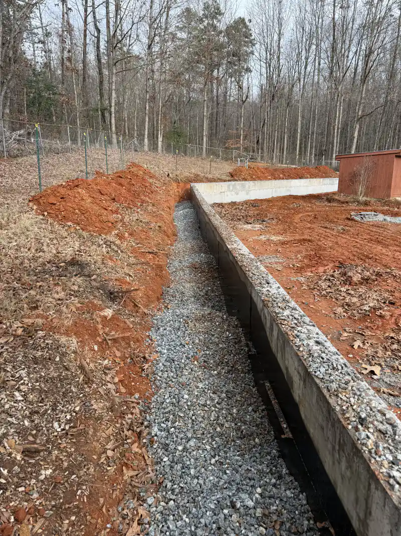 A foundation wall coated with waterproofing membrane, with perforated drainage pipe bedded in gravel along the footing.