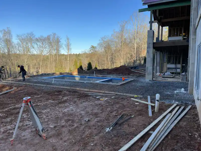 A foundation and pool shell under construction, with a surveying tripod set up on site.