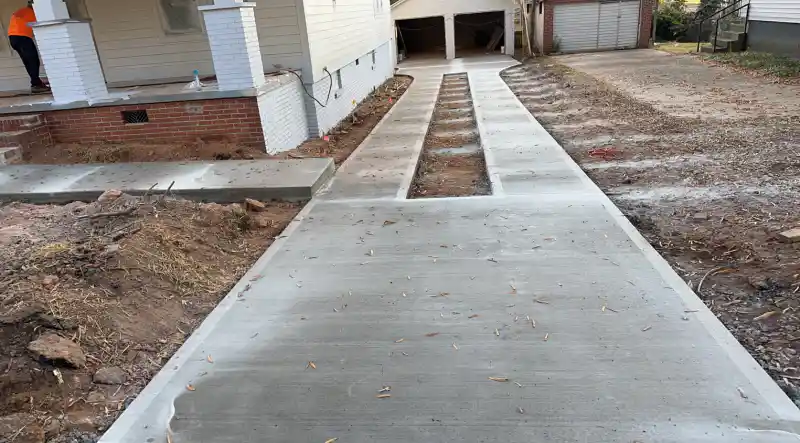 A newly poured concrete walkway and driveway strips beside a house, with open trenches between the strips.