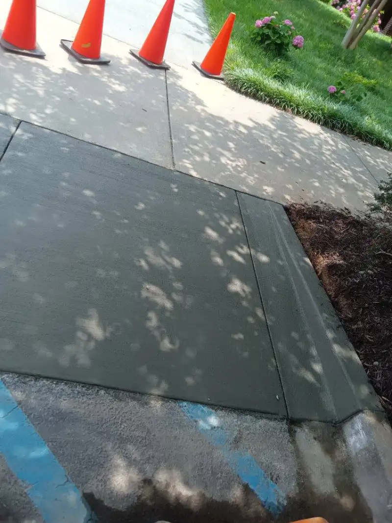 A newly poured public sidewalk section with traffic cones set out and survey marks on the adjacent asphalt.