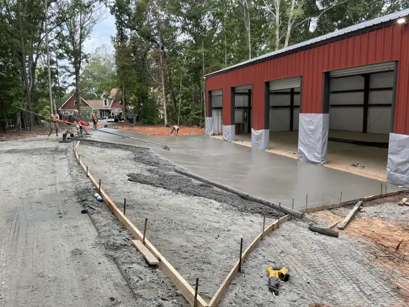 A concrete slab being poured inside a red metal building, with a crew working the surface and a pump truck alongside.