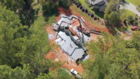 An aerial view of a residential foundation being poured with a concrete pump truck alongside.