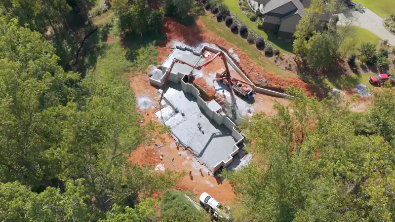 An aerial view of a residential foundation being poured, with a concrete pump truck positioned alongside the formed footprint.